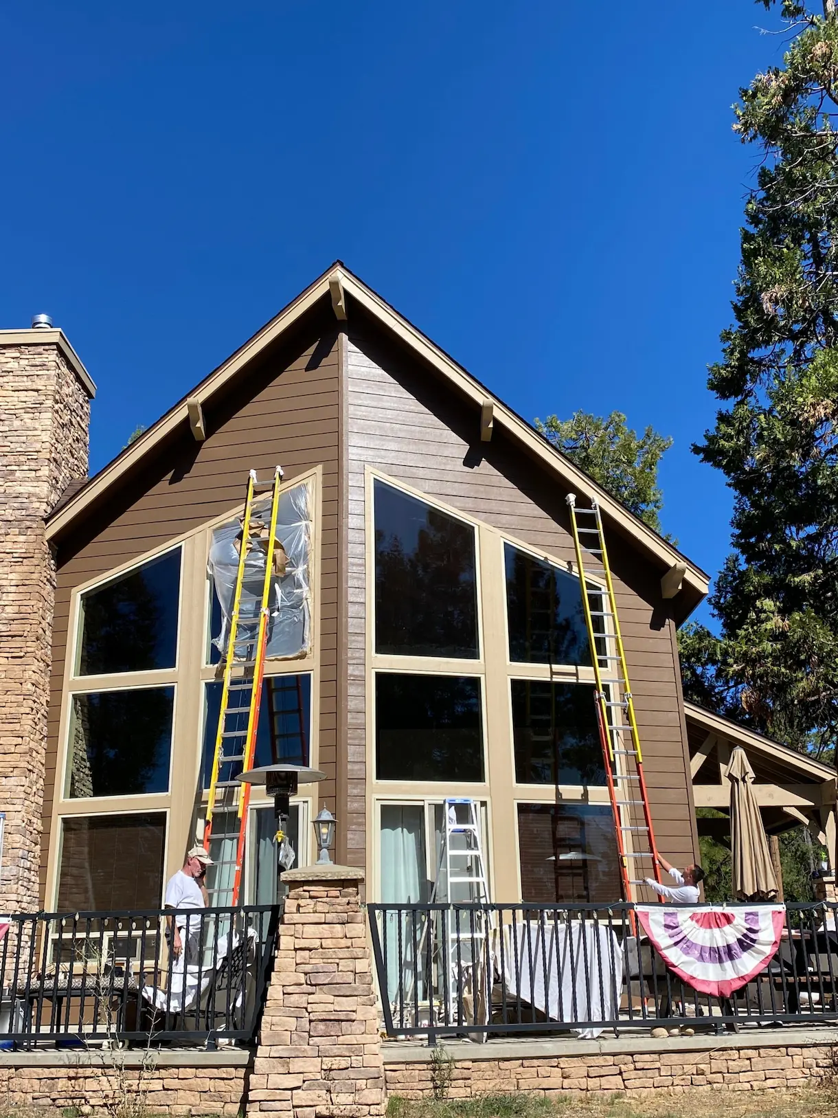 A-frame home exterior being painted with ladders in place