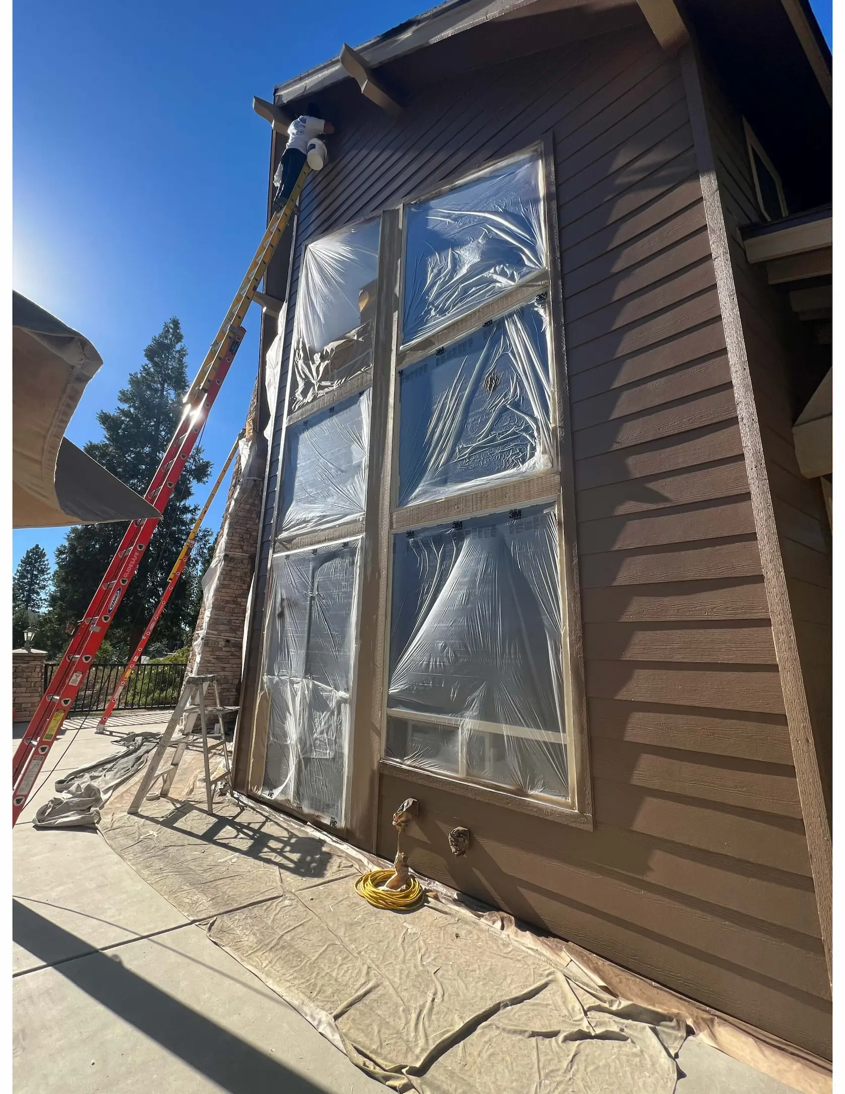 Dark lap siding and window trim being repainted with masking in place